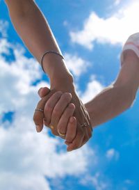 Close-up of couple holding hands against blue sky