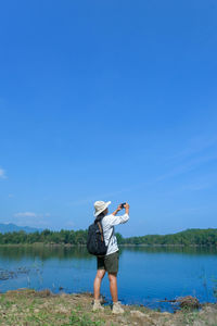 Rear view of woman standing by lake against blue sky