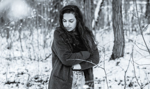Portrait of young woman standing on tree trunk during winter