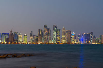 Illuminated city by sea against clear sky at night