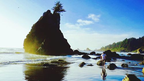 People on rock by sea against clear sky
