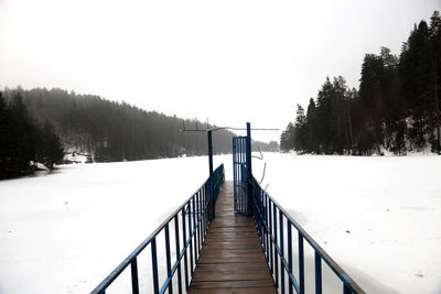 Footbridge amidst snow covered trees against clear sky