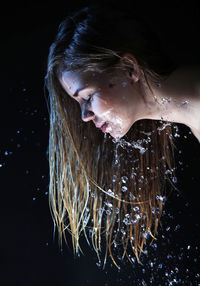 Side view of woman with water on face against black background