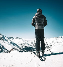 Rear view of man standing on snowcapped mountain against clear blue sky