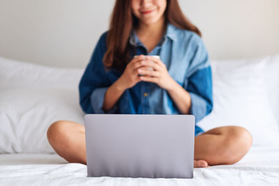 Midsection of woman using laptop on bed at home