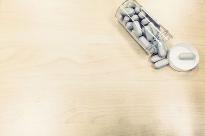High angle view of open bottle of pills on wooden table