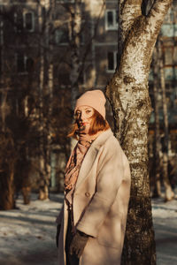 Portrait of woman standing by tree trunk during winter