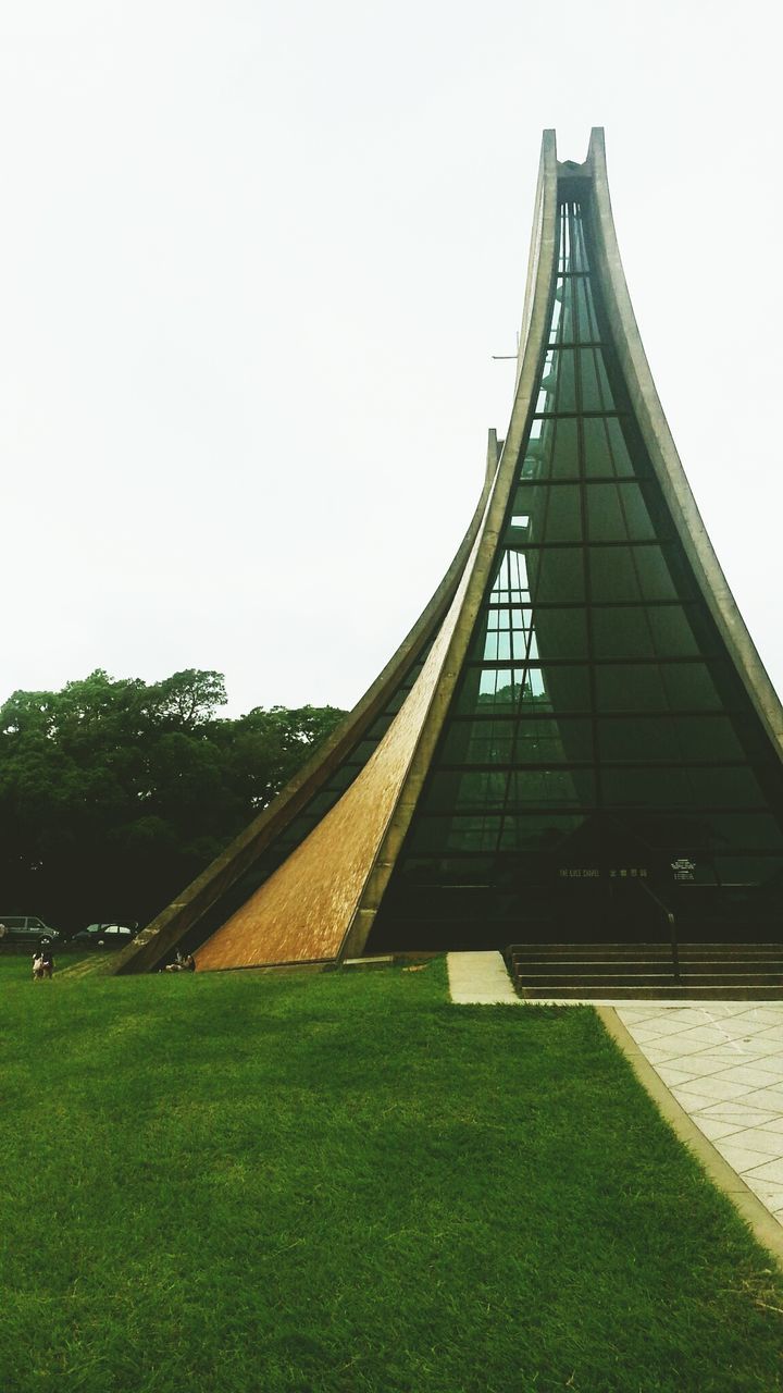 architecture, clear sky, built structure, building exterior, grass, copy space, day, sky, tree, city, building, outdoors, green color, no people, growth, road, sunlight, low angle view, field, residential structure