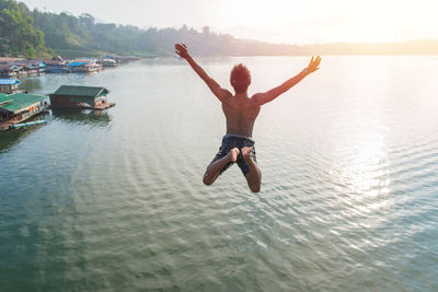 Rear view of man jumping in river during sunny day