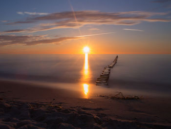 Stepping stones in sea against sky during sunset