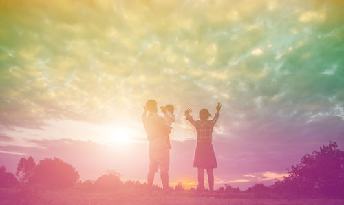 Low angle view of friends standing against sky during sunset