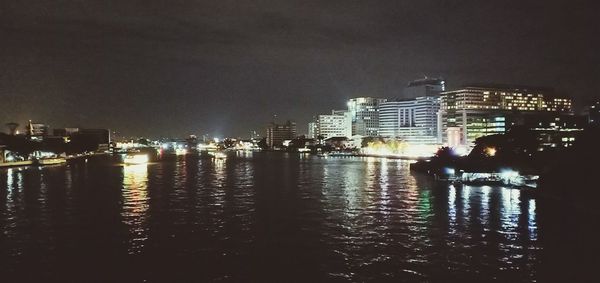 Illuminated buildings by river against sky at night