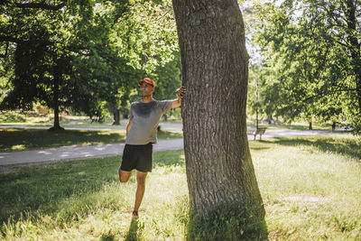 Man doing stretching while standing near tree at park on sunny day