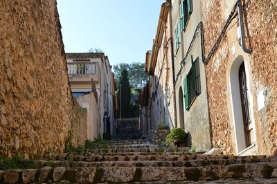 Narrow alley amidst old buildings in town against sky. old town of pollença, majorca, spain.