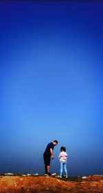 Father with daughter standing on cliff by sea against clear blue sky during sunny day