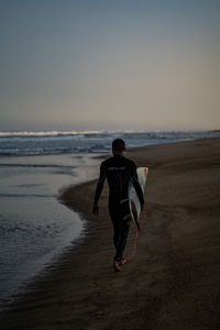 Rear view of man on beach against sky during sunset