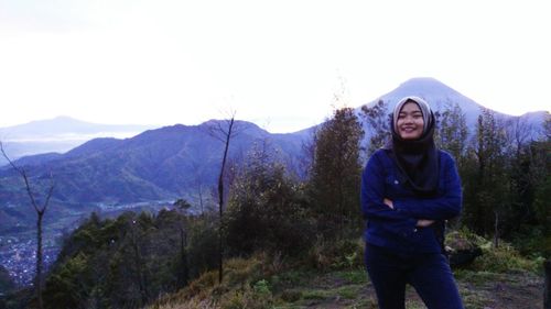 Portrait of smiling young woman standing on mountain against sky