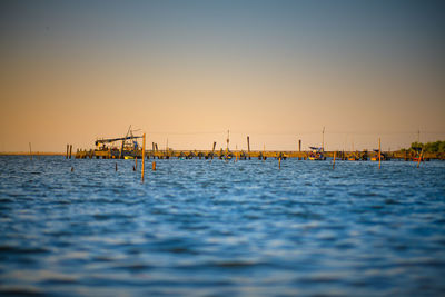 Sailboats in sea against clear sky during sunset