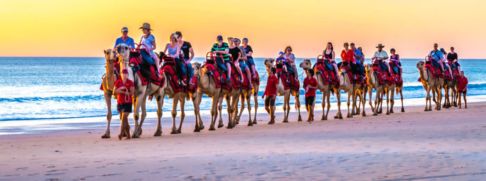 People on beach against clear sky during sunset