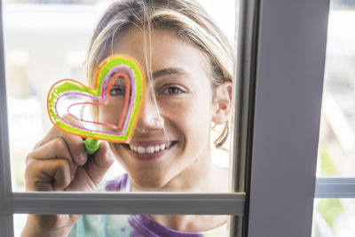 Portrait of smiling woman drawing heart shape on glass window