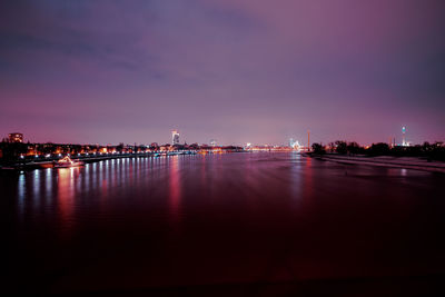 Illuminated buildings by river against sky at dusk