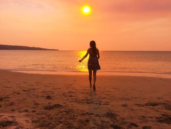 Rear view of woman walking at beach during sunset