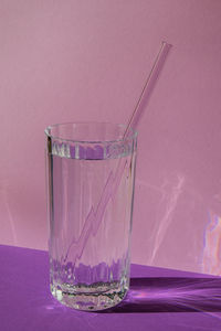 Reusable glass straws in glass with water on purple violet background eco-friendly drinking straw