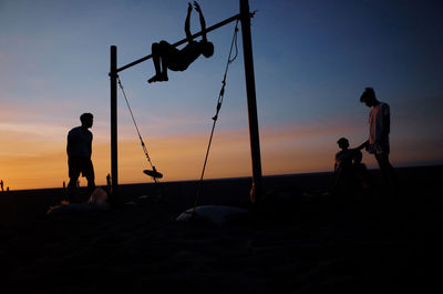 Silhouette people on beach against sky during sunset