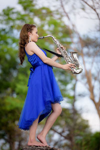 Side view of woman wearing blue dress playing saxophone at public park