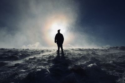 Rear view of silhouette man standing in sea against sky