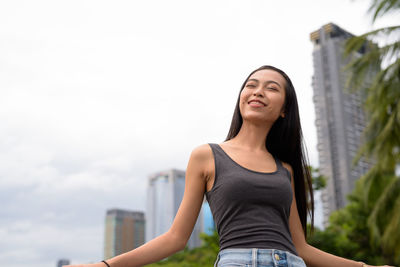 Portrait of smiling woman standing against sky in city