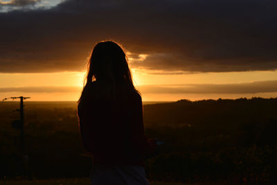 Silhouette woman standing on field against sky during sunset