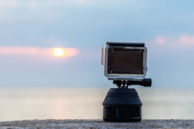 Close-up of coin-operated binoculars by sea against sky during sunset