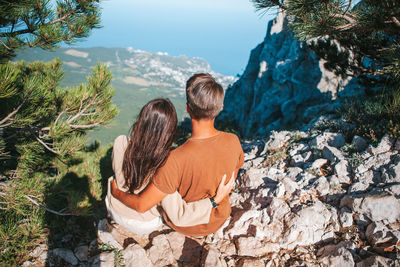 Rear view of couple sitting on rock looking at view