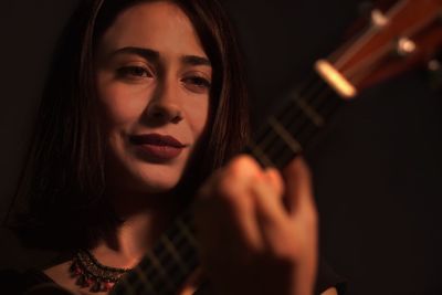 Close-up of woman playing guitar against black background