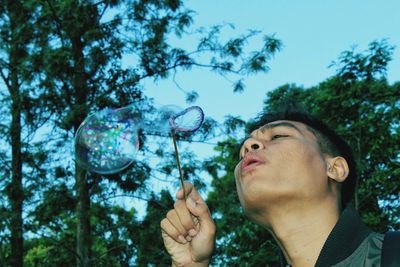 Low angle view of man making bubbles tree against sky