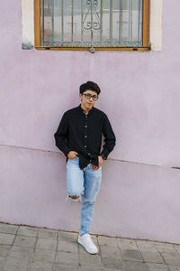 Young transgender man leaning on a wall while posing outdoors on the street.