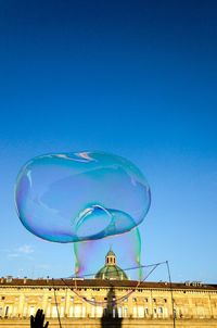 Low angle view of bubbles against clear blue sky