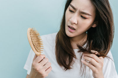 Worried woman holding brush with hair against blue background