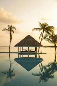 Reflection of gazebo and palm trees in infinity pool against sky