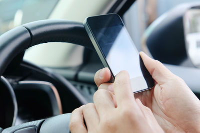 Cropped hand of person using mobile phone in car