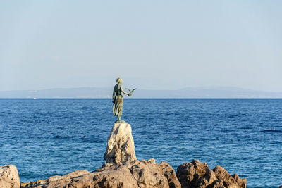 Statue of maiden with seagull on rocky coast in opatija, croatia.