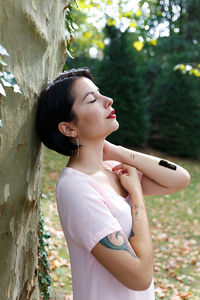 Side view of young woman standing against tree