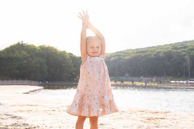 Portrait of young woman with arms raised standing at beach