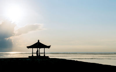 Silhouette lifeguard hut on beach against sky during sunset