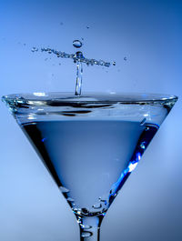 Close-up of water splashing on glass against blue background