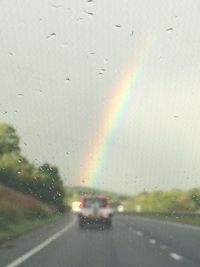 Cars on country road against rainbow in sky