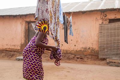 Side view of woman in traditional clothing drying laundry against old house