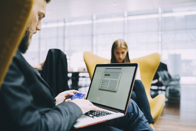 Businessman holding credit card while using laptop at airport