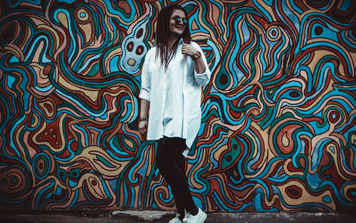 Full length of young woman standing against graffiti wall